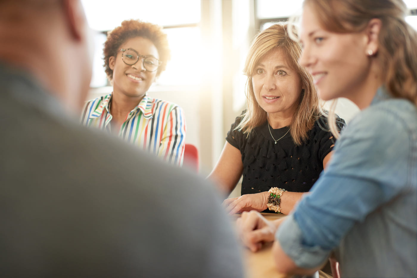 A female manager having a discussion at a table with 3 other employees.