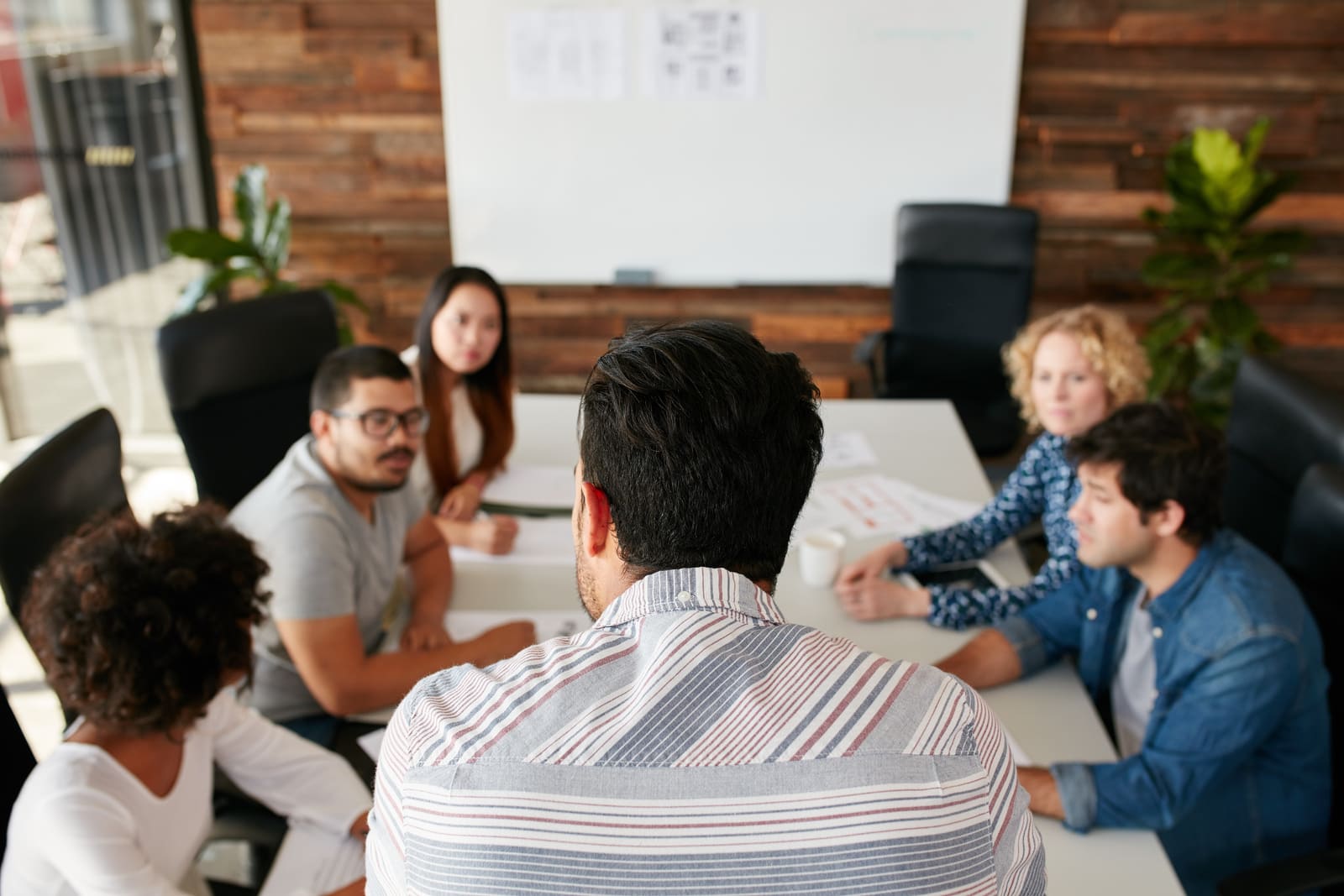 A group of professionals in an office having a discussion with one person standing in the front.